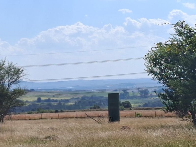 A scenic view of the surrounding landscape featuring open fields, distant hills, and existing wire fencing with a water tank on the property.