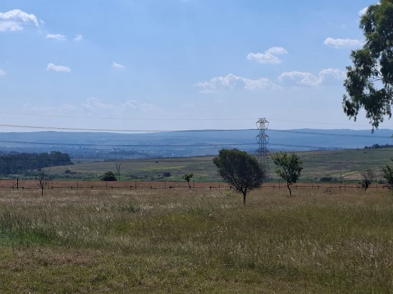 A wide-angle view of the vacant residential land featuring natural grass, scattered trees, wire fencing, and distant mountain views under a clear sky.