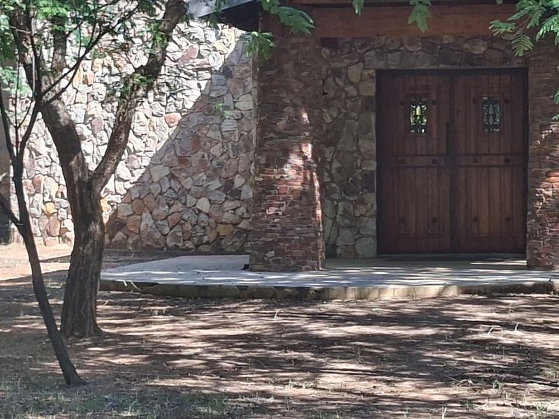 Front entrance featuring rustic stone cladding, a concrete porch, and double wooden doors set within a natural, tree-shaded landscape.