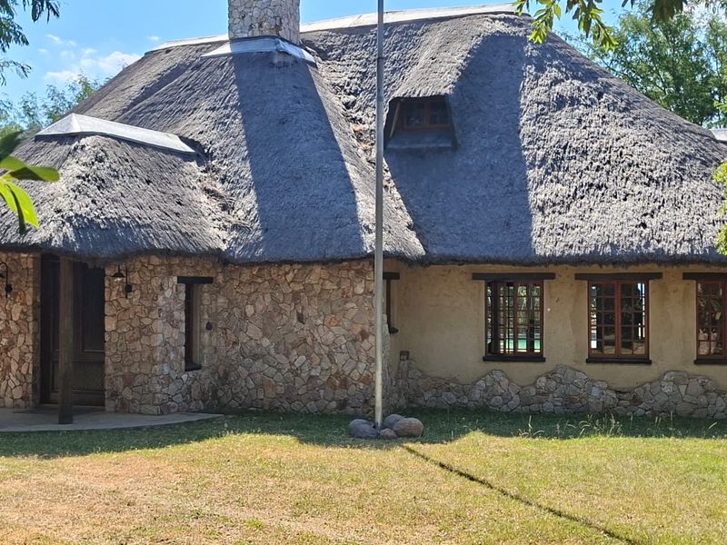 A charming residential property featuring a traditional thatch roof, stone cladding, and timber-framed windows, set within a well-maintained garden.