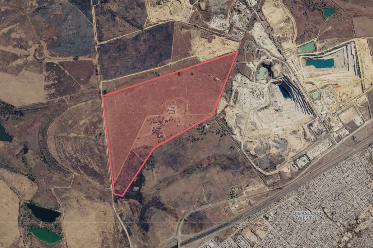 An aerial view of a large, vacant residential land parcel with clear boundary markings, situated near industrial and residential areas.