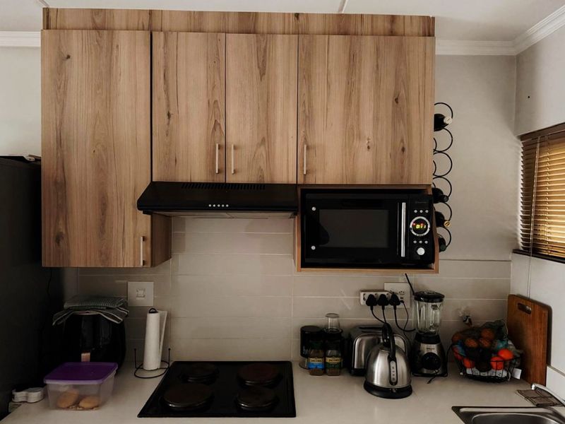 A functional kitchen area featuring wood-look cabinetry, a built-in microwave housing, an electric hob, and a clean subway tile backsplash.