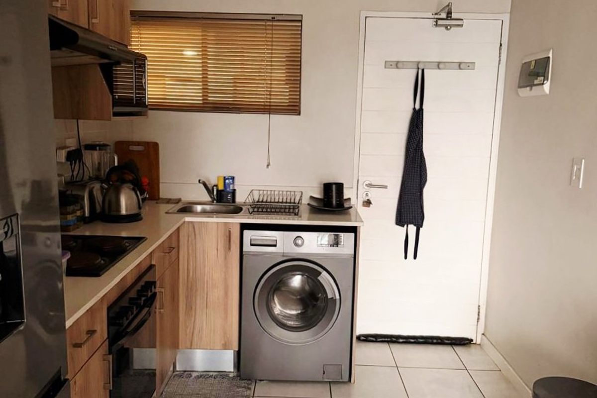 A functional kitchen featuring wood-look cabinetry, tiled flooring, integrated oven, and a dedicated space for a washing machine.