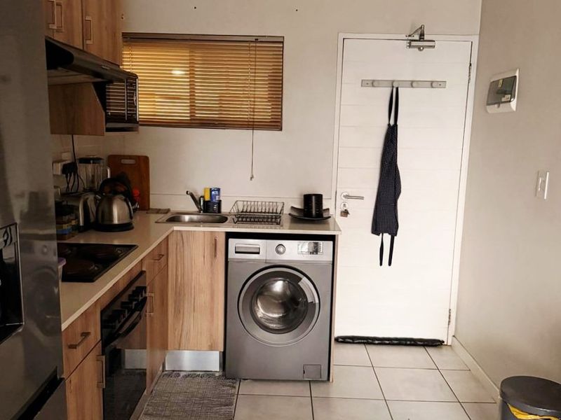 A functional kitchen featuring wood-look cabinetry, tiled flooring, integrated oven, and a dedicated space for a washing machine.