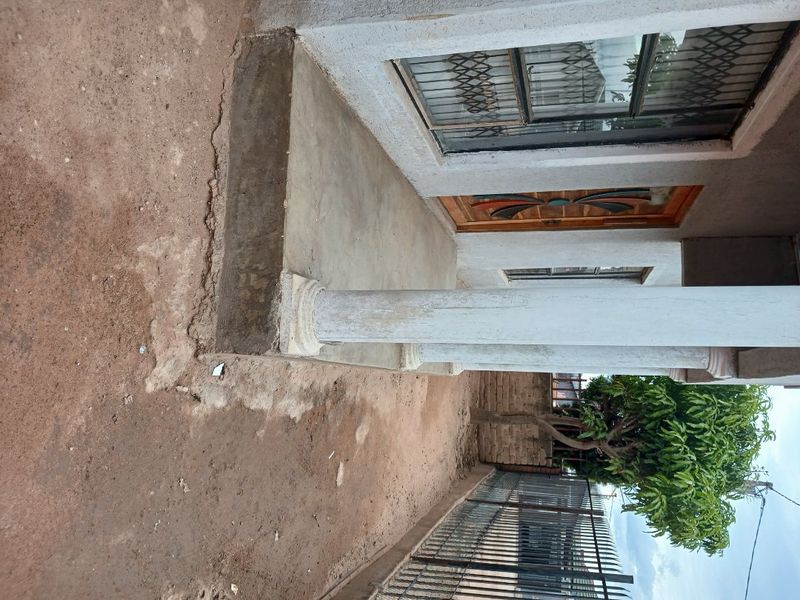 Front entrance area featuring a concrete porch with a decorative column, security gate, and metal perimeter fencing.