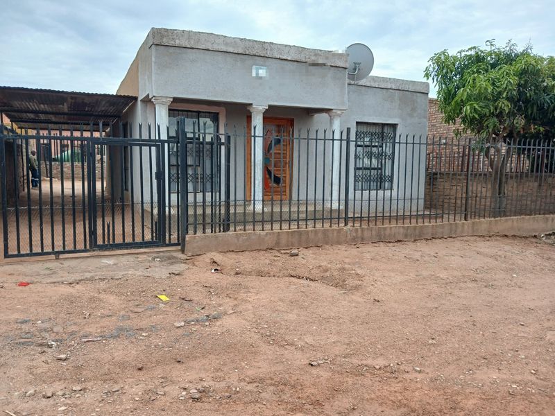 Front view of a single-story house featuring a covered entrance with concrete columns, metal security fencing, and an attached carport.