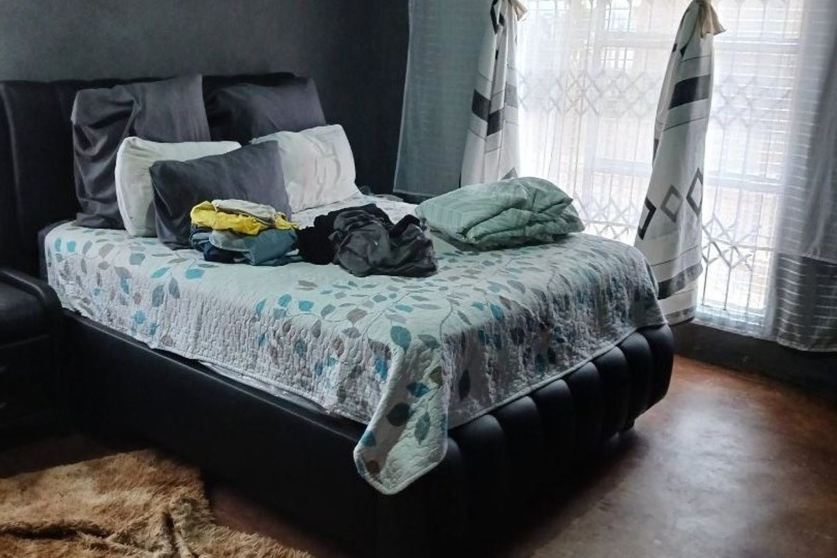 A bedroom featuring dark painted walls, concrete flooring, and a window fitted with a security gate.