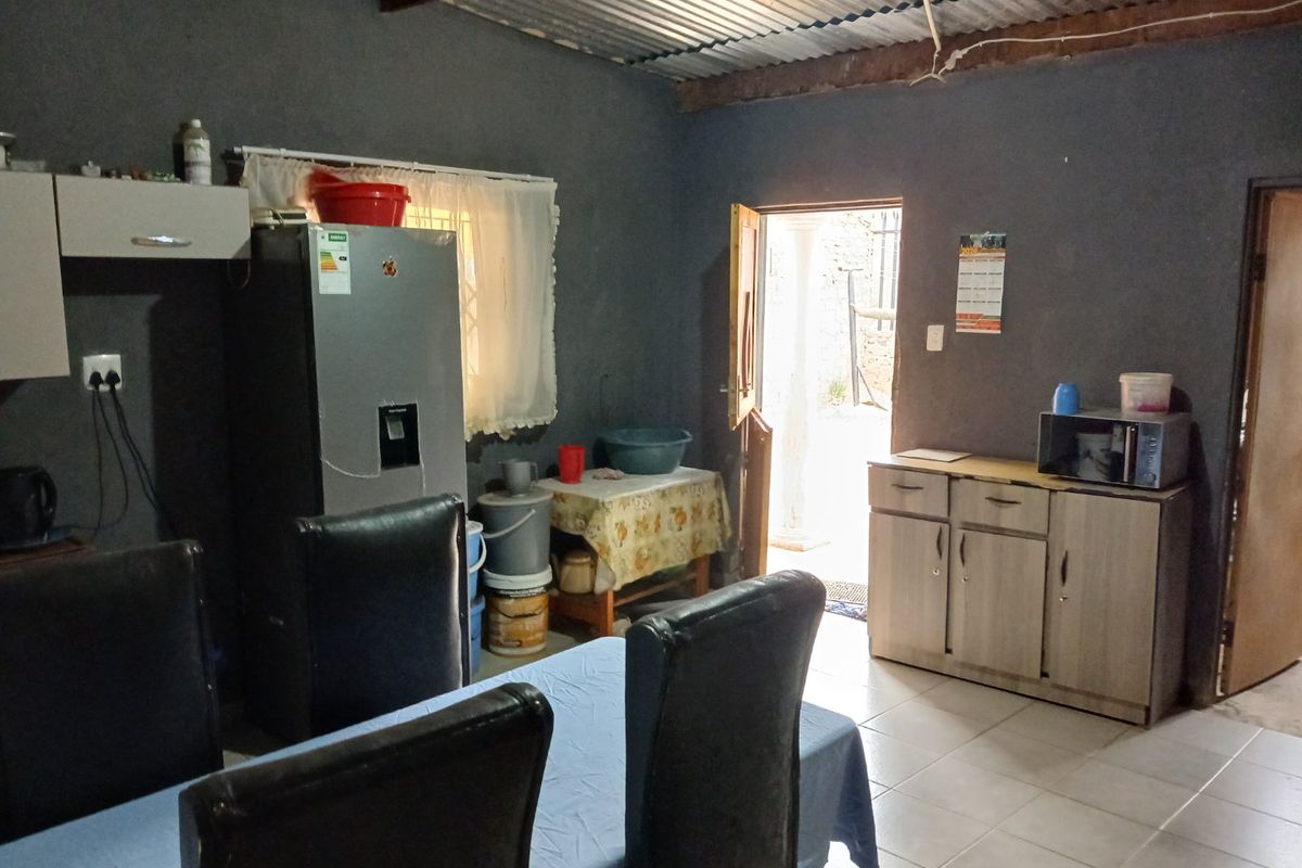 A functional kitchen area featuring tiled floors, built-in cabinetry, and an exposed corrugated iron ceiling with timber beams, providing direct access to the exterior.