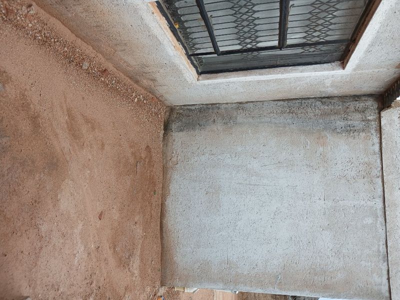 An exterior rear area featuring a concrete base and a security gate, currently in an unfinished state with exposed soil.