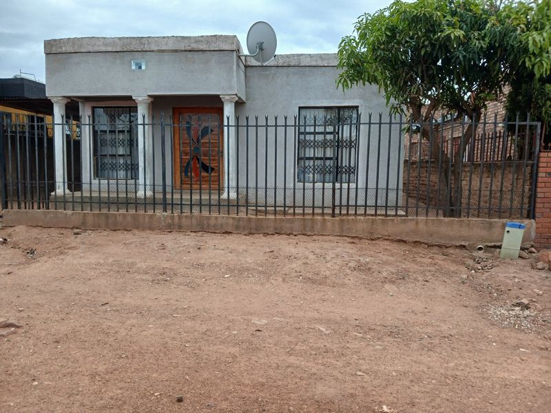Front view of a single-story house featuring a metal security fence, concrete columns, and a wooden entrance door with decorative glass.