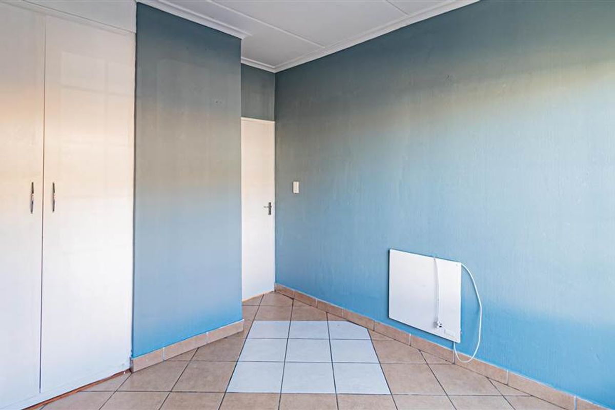 An empty bedroom featuring built-in cupboards, tiled flooring, and a wall-mounted heater, offering a blank canvas for personalization.