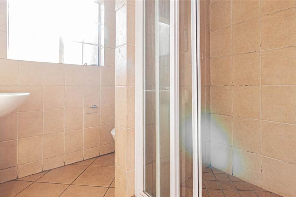 A functional bathroom featuring a pedestal basin, a shower enclosure, and neutral tiled finishes throughout.