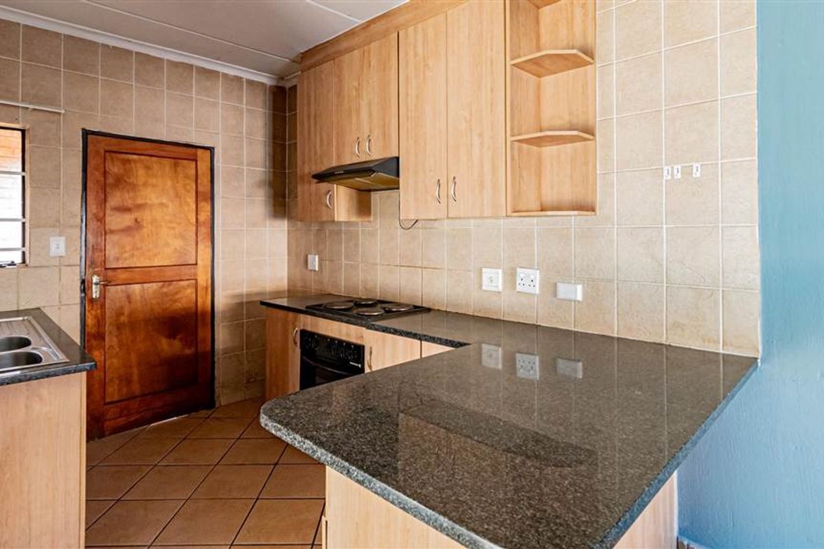 A functional kitchen featuring granite countertops, built-in cabinetry, an integrated oven and hob, and tiled finishes throughout.