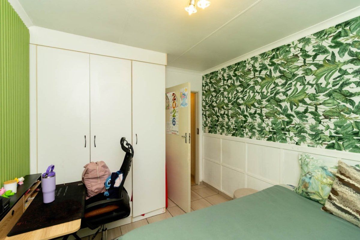 A bedroom featuring built-in wardrobes, tiled flooring, and decorative wainscoting with botanical wallpaper.