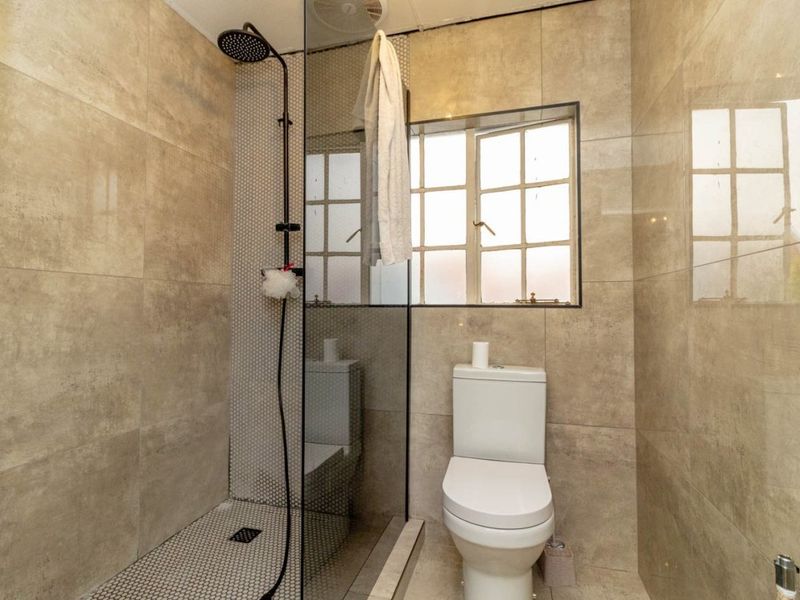 Modern bathroom featuring a walk-in shower with a rain shower head, glass screen, and neutral floor-to-ceiling tiling.