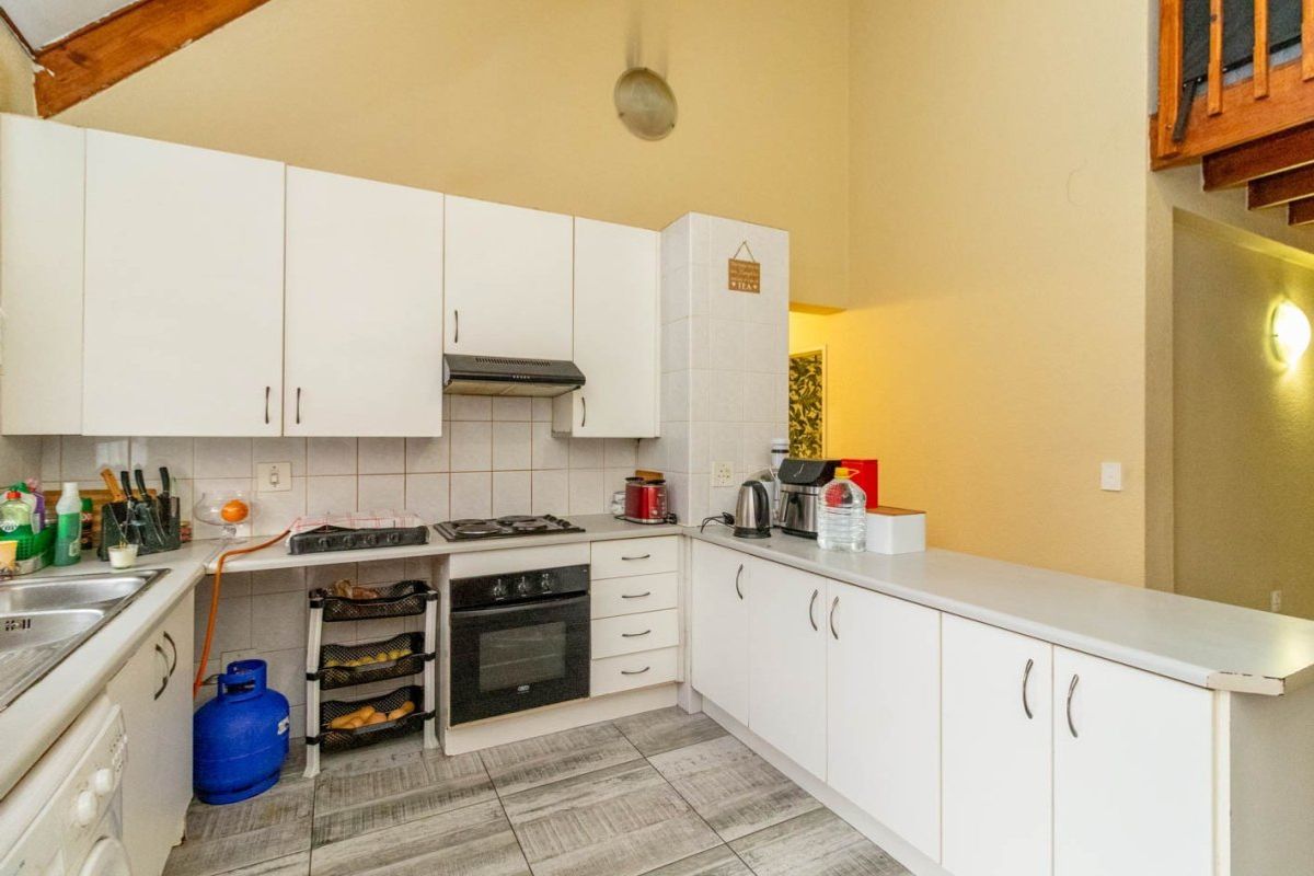 Functional kitchen featuring white cabinetry, built-in oven, gas hob, extractor fan, and tiled flooring with a high vaulted ceiling.