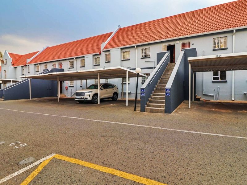 Exterior view of an apartment complex featuring covered parking bays, external staircases, and a tiled roof structure.