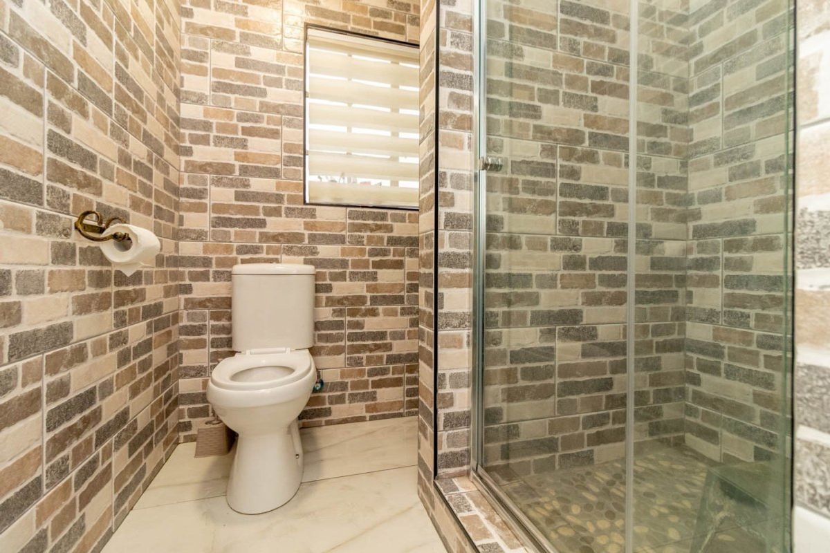A compact bathroom featuring brick-style wall tiles, a modern toilet, and a glass-enclosed shower with pebble-style floor tiling.