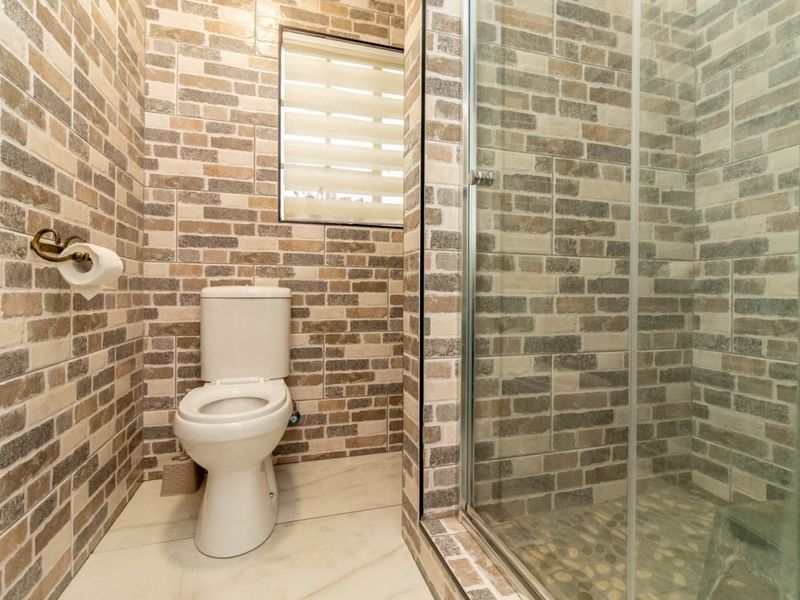 A compact bathroom featuring brick-style wall tiles, a modern toilet, and a glass-enclosed shower with pebble-style floor tiling.