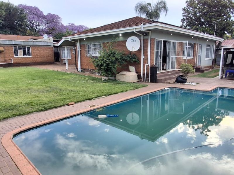 Rear exterior view of the house featuring a swimming pool, paved patio area, and a spacious lawn.