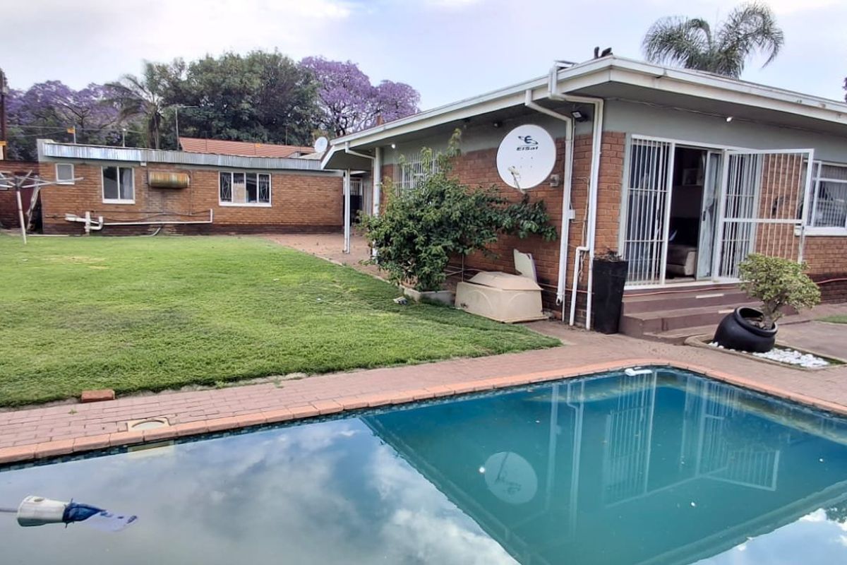 Rear view of the property featuring a swimming pool, paved surround, and brick exterior walls with security gates and sliding door access.