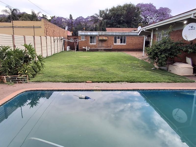 A rear garden area featuring a swimming pool, brick paving, and a precast boundary wall with electric fencing, adjacent to the main house structure.