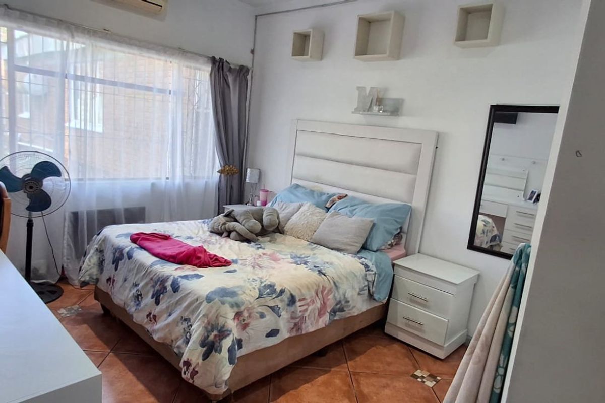 A bedroom featuring tiled flooring, an air conditioning unit, and built-in wall shelving, with large windows providing natural light.
