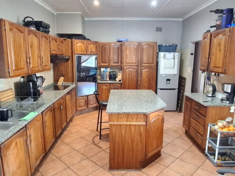 A functional kitchen featuring extensive wooden cabinetry, granite countertops, a central island, and tiled flooring, offering a traditional layout with ample storage space.