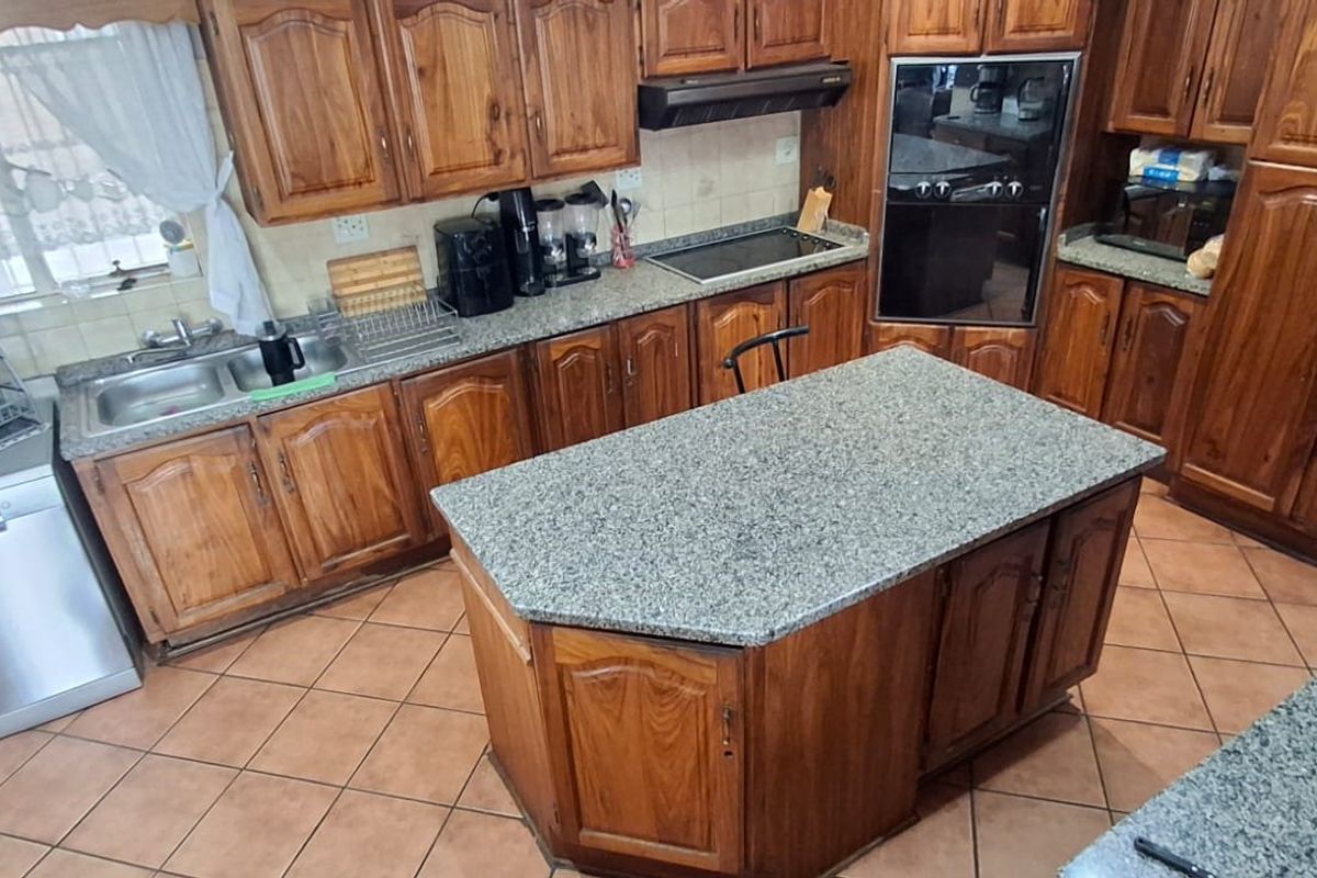 A functional kitchen featuring extensive wooden cabinetry, granite countertops, a central island, and built-in appliances with tiled flooring throughout.
