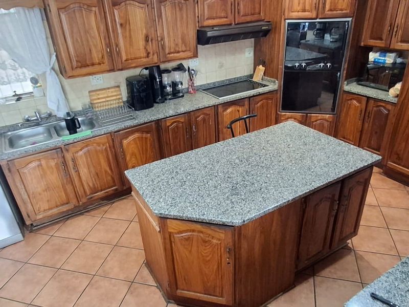 A functional kitchen featuring extensive wooden cabinetry, granite countertops, a central island, and built-in appliances with tiled flooring throughout.
