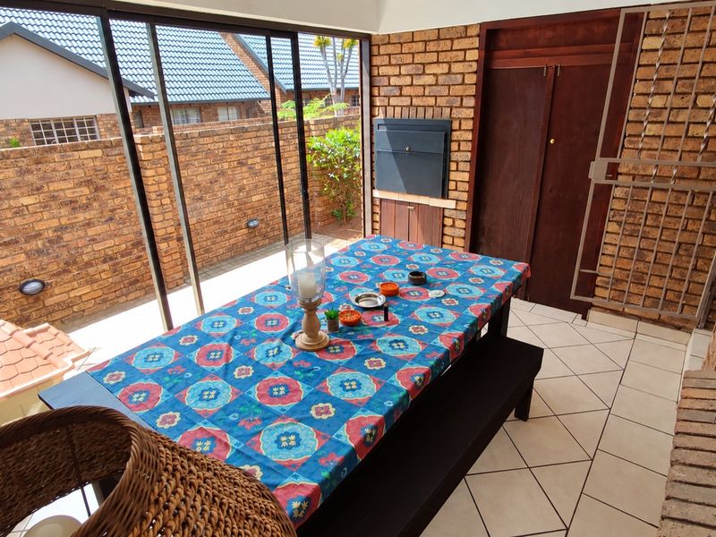Enclosed patio area featuring exposed brick walls, tiled flooring, and a built-in braai, providing a versatile space for outdoor dining and entertainment.
