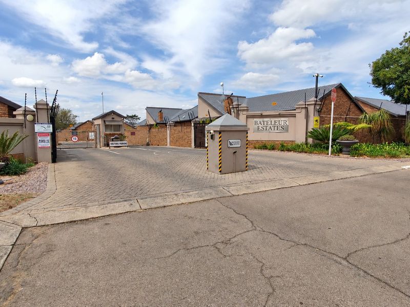 The main entrance to Bateleur Estates featuring a secure gated access point, paved driveway, and perimeter brick walling with electric fencing.