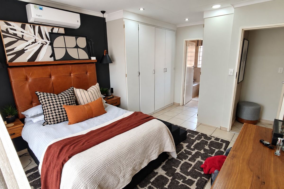 A well-maintained bedroom featuring built-in cupboards, tiled flooring, recessed lighting, and an air conditioning unit, with direct access to an en-suite bathroom.