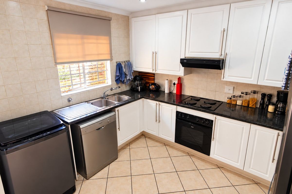 A functional kitchen featuring white cabinetry, granite countertops, built-in oven and hob, and tiled finishes, providing a clean and practical workspace.