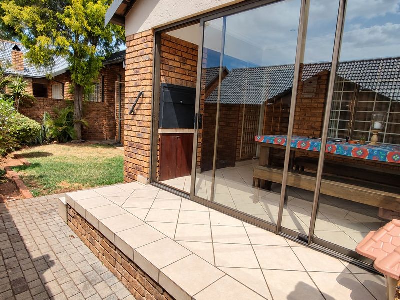 Covered patio area featuring a built-in braai, tiled flooring, and large sliding glass doors providing access to the interior living space.
