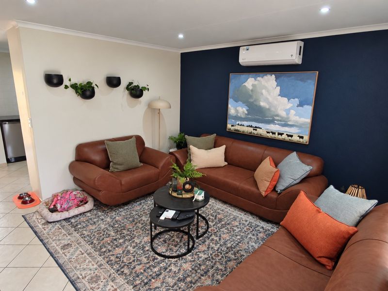 A well-maintained living room featuring tiled flooring, recessed downlighting, and a wall-mounted split-system air conditioner, accented by a bold navy feature wall.