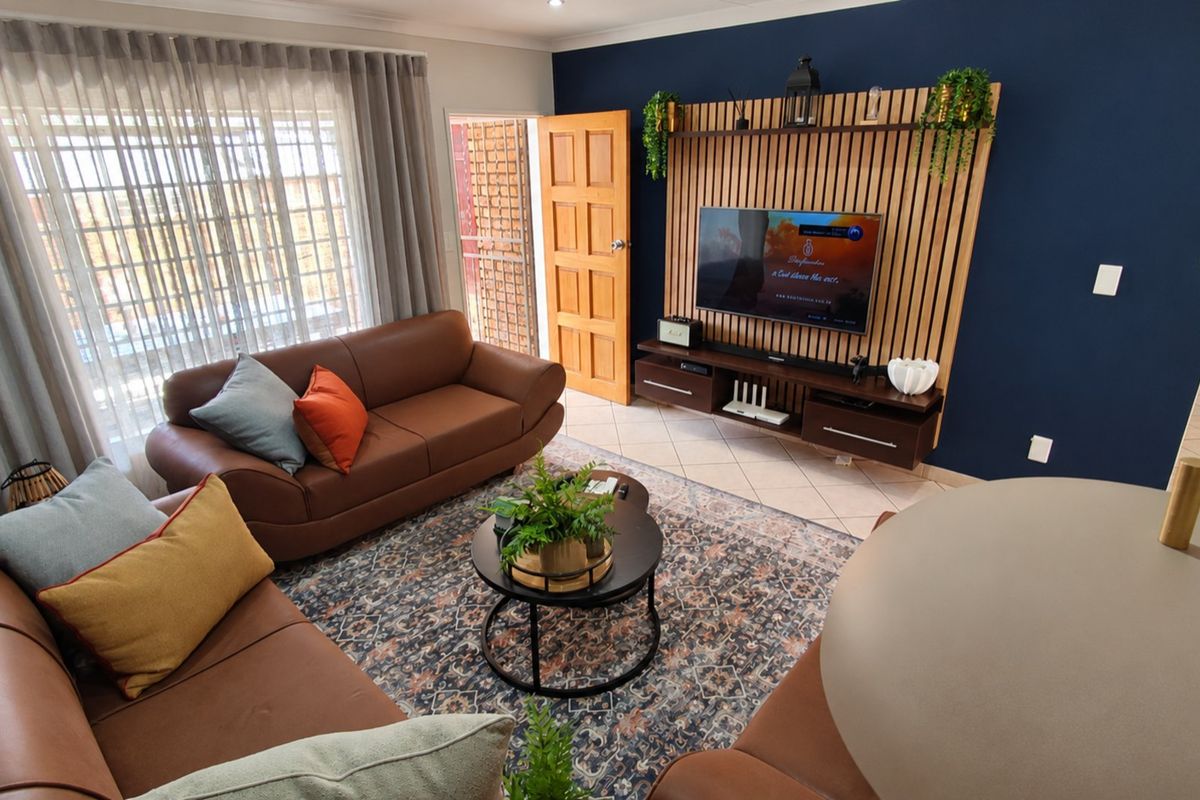 A well-maintained living room featuring a modern slatted timber feature wall, tiled flooring, and recessed lighting, creating a warm and inviting atmosphere.