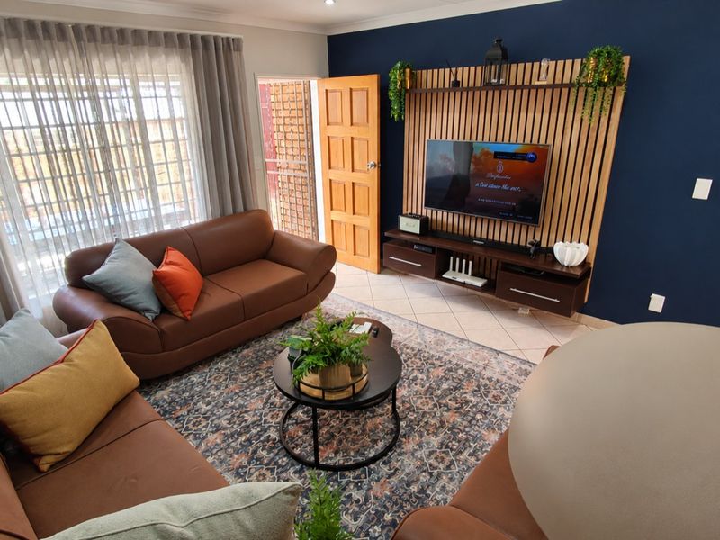 A well-maintained living room featuring a modern slatted timber feature wall, tiled flooring, and recessed lighting, creating a warm and inviting atmosphere.