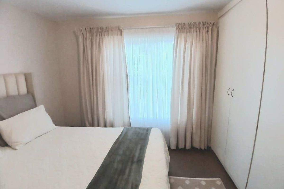 A bedroom featuring a built-in wardrobe and window with curtain tracks, offering a neutral and functional space.