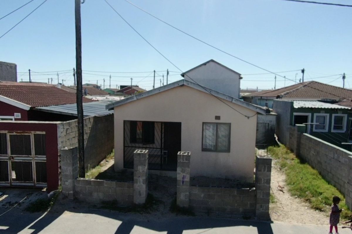 Front elevation of a detached house featuring a concrete block boundary wall, security gate, and security bars on windows.