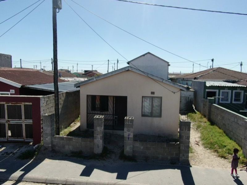 Front elevation of a detached house featuring a concrete block boundary wall, security gate, and security bars on windows.