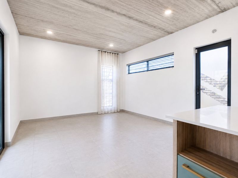 Modern open-plan living area featuring an exposed concrete ceiling, tiled floors, and sleek built-in cabinetry with stone countertops, offering a bright and contemporary space.