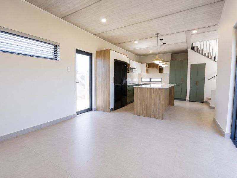 Modern open-plan kitchen and living area featuring a central island, sleek cabinetry, tiled floors, and an exposed concrete ceiling with integrated lighting.