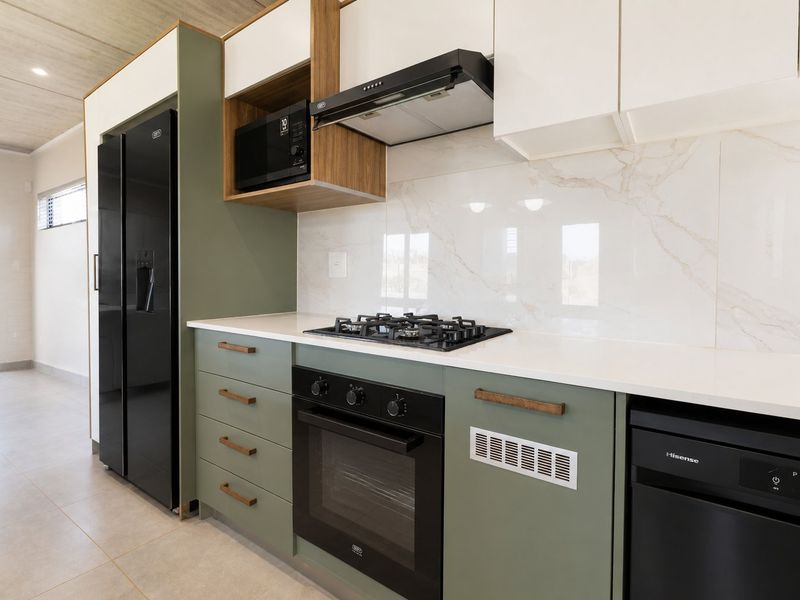 Modern kitchen featuring sage green cabinetry, stone countertops, marble-look splashback, and integrated appliances including a gas hob, oven, and extractor fan.
