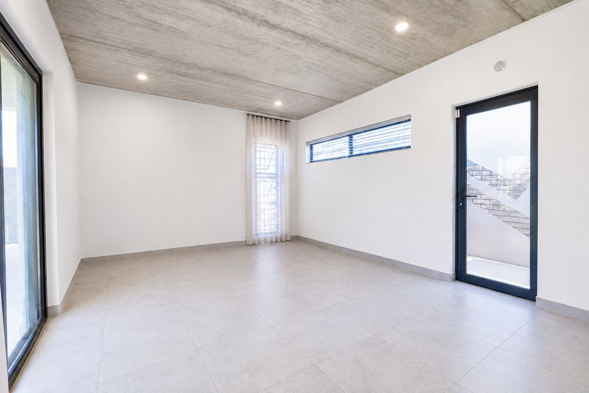 A bright, modern, and empty living space featuring an exposed concrete ceiling, large tiled floors, and direct access to outdoor areas through glass doors.