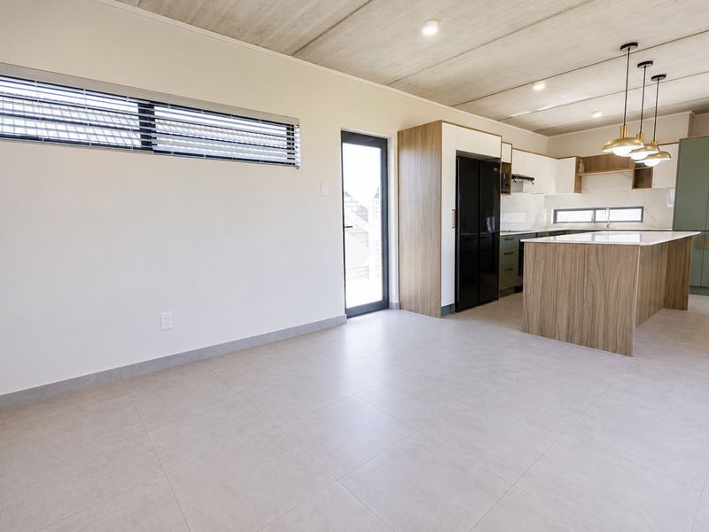Modern open-plan kitchen and living area featuring a central island, sleek cabinetry, tiled floors, and an exposed concrete ceiling with contemporary pendant lighting.