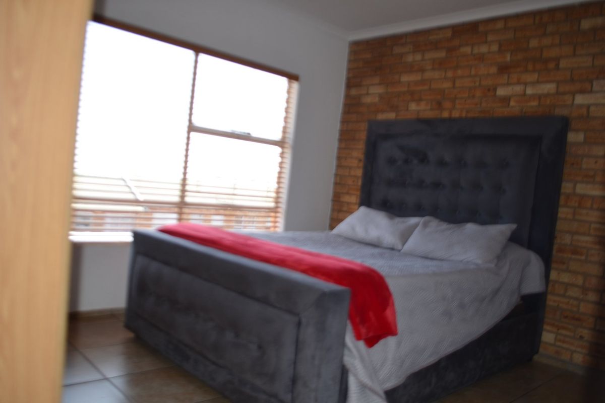 A bedroom featuring an exposed brick accent wall, large window for natural light, and tiled flooring.