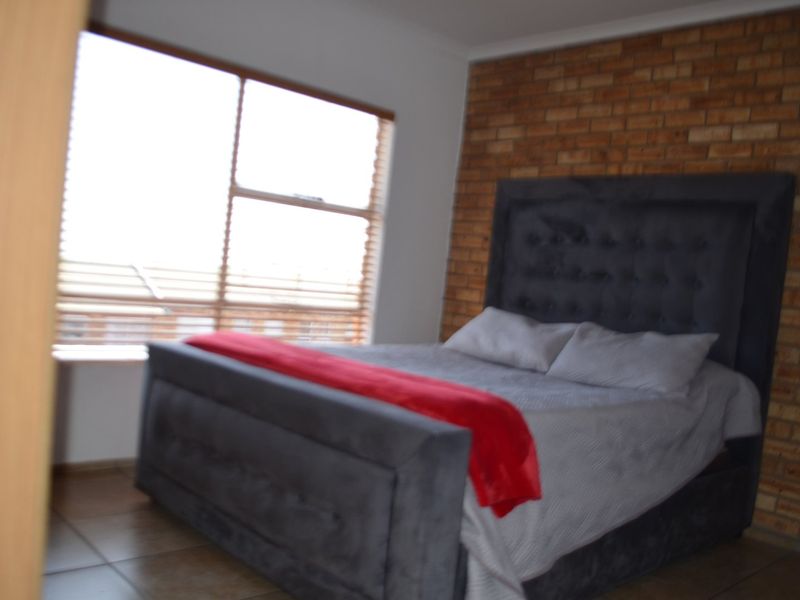 A bedroom featuring an exposed brick accent wall, large window for natural light, and tiled flooring.
