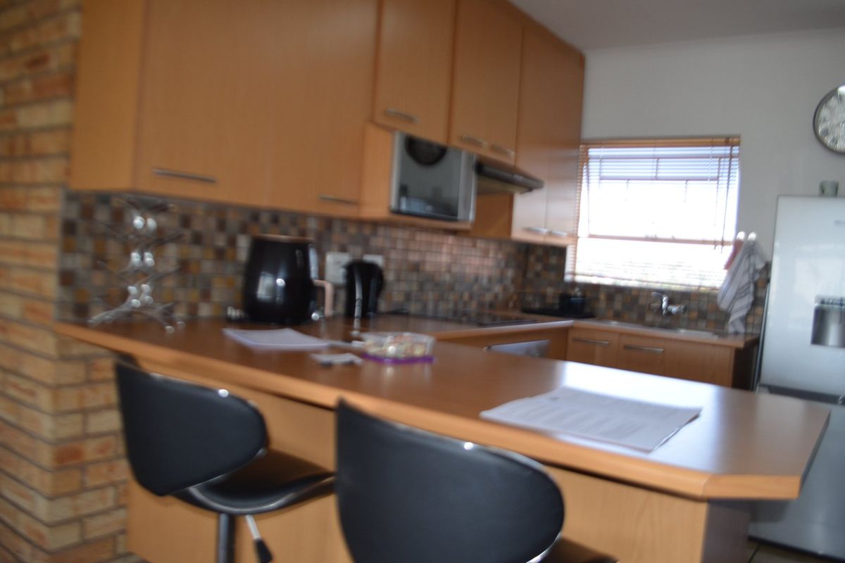 A functional kitchen featuring light wood cabinetry, a mosaic tile backsplash, a breakfast bar, and a distinctive brick feature wall.