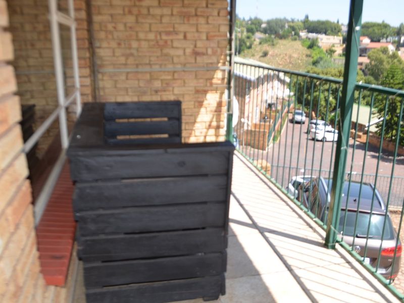 A balcony featuring brick walls, tiled flooring, and a metal railing, offering an elevated view of the surrounding area.